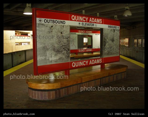 Quincy Adams, Cascaded - A receding series of three platform signs are visible, through a center cut-out in each, at the Quincy Adams MBTA station