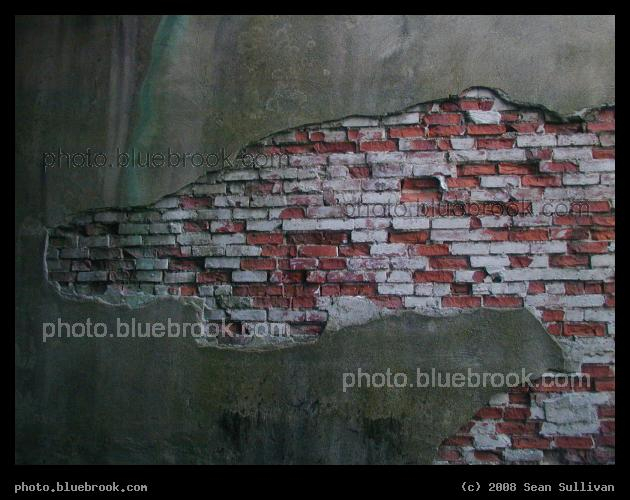 Bricks Revealed - A brick wall on the side of a building, partly covered by concrete, copper streaks and plant growth, Brookline MA
