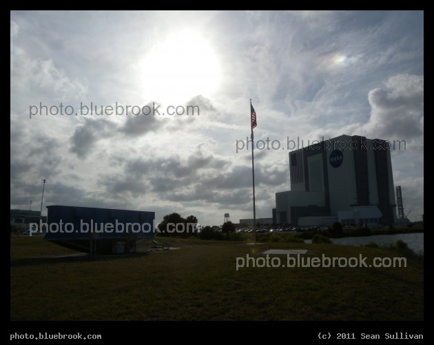Clouds over Press Site - The sun and clouds over the Kennedy Space Center press site, with the back side of the countdown clock (left) and nearby Vehicle Assembly Building (right), shortly after the launch of Atlantis on flight STS-132