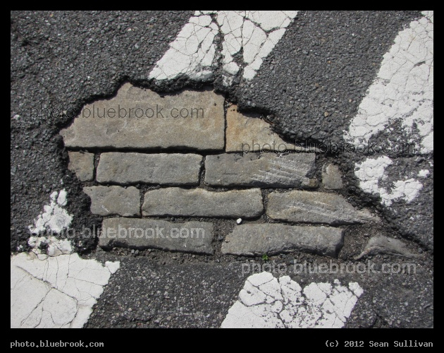 Revealed - In a crosswalk, a stone underlayer of a street is revealed under the asphalt. Somerville, MA
